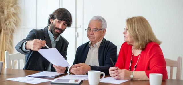 Bearded Man Showing Papers to a Couple Sitting at the Table