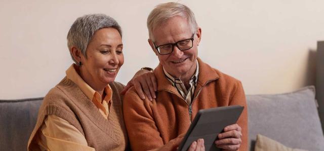 Retired Man and Woman Sitting Sofa While looking at a Tablet Device